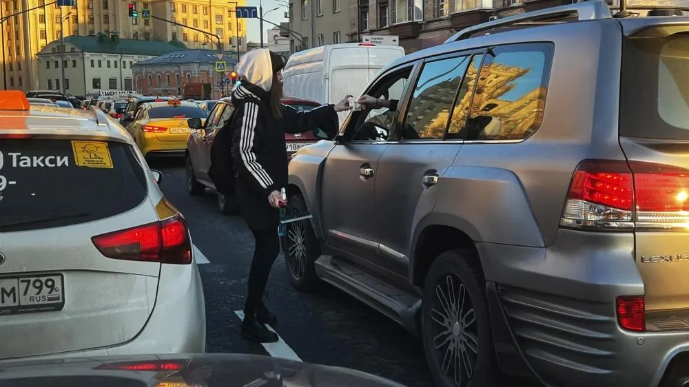 Девушка получает деньги от водителя за мытье фар его автомобиля, пока он стоял в пробке в Москве