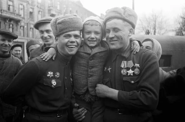 Советские воины-орденоносцы, участники боев за освобождение Одессы держат на плечах юного одессита. На снимке — военнослужащие отдельной армейской разведывательной роты 6-й армии 3-го Украинского фронта: разведчик ефрейтор Михаил Сысоев (справа) и командир разведывательного взвода лейтенант Андрей Васильков (слева)